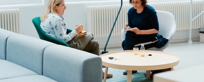 two woman sits on sofa chairs inside house